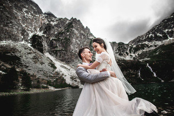 Beautiful wedding photosession. The groom circles his young bride, on the shore of the lake Morskie Oko. Poland