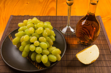 large brush of green grapes in a ceramic plate, a decanter and a glass of wine and cheese