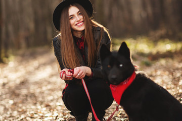 Young girl with a dog walking in the autumn park. Girl has a beautiful black hat.