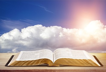 Open book on old wooden table on sky background sunlit