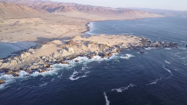 Las Tortolas beach aerial footage at Atacama Desert the sunset ray lights illuminate this amazing and idyllic beach in the middle of the desert, an arid awe landscape crashed by Pacific Ocean waters