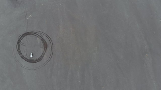 Aerial Lockdown: Car Parked In Middle Of Tire Driven Circle In Sand in Solheimasandur, Iceland