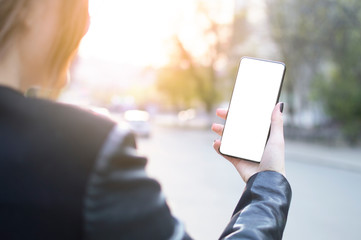 the girl is holding a frameless smartphone against the background of the city and the sunset, and his screen is lit up creating free space