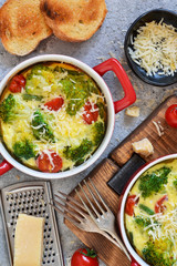 Casserole with broccoli, tomatoes and parmesan on a concrete background. View from above.