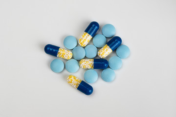 Blue and yellow pills and capsules on light grey background