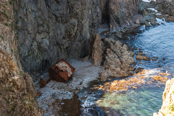 An old shipwrecked ship stands on the shore at the foot of a rocky cliff. Cape Briner. Primorsky Krai. Russia.