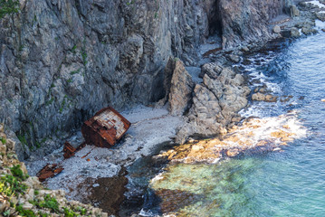 An old shipwrecked ship stands on the shore at the foot of a rocky cliff. Cape Briner. Primorsky...