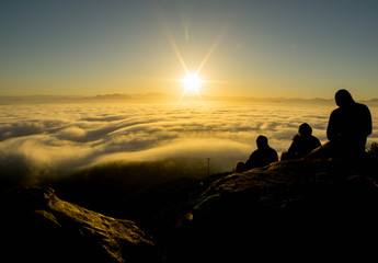 Naklejka na ściany i meble silhoutettes of people oberserving the sunrise from a mountain through the clouds - Cowles Mountain San Diego