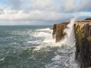 Powerful wave hits mini cliff, West coast of Ireland, county Clare. Cloudy sky,