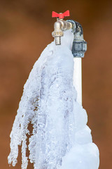 Frozen faucet. Brown background.