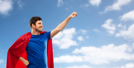 Fototapeta na wymiar super power and people concept - happy young man in red superhero cape over blue sky and clouds background