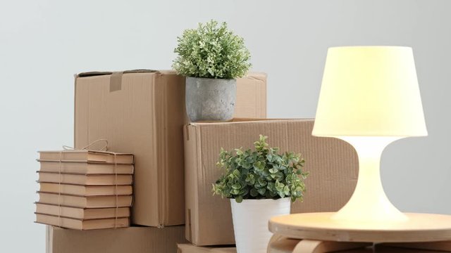 A white table lamp turns on and off against the background of cardboard boxes. The concept of moving to a new home.