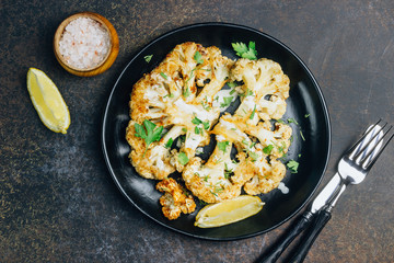Fried cauliflower steak with greens and spices on dark background.