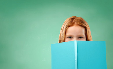 education, school and people concept - red haired student, girl hiding behind book over green chalk...