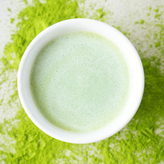 Flat-lay of bawl with Japanese Matcha tea over scattered  powder tea on concrete background with copy space, top view.