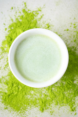 Flat-lay of bawl with Japanese Matcha tea over scattered  powder tea on concrete background with copy space, top view.