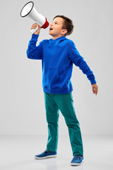 childhood, expressions and people concept - smiling boy in blue hoodie speaking to megaphone over grey background