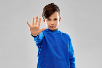 restriction, prohibition and children concept - boy in blue hoodie making stopping gesture over...