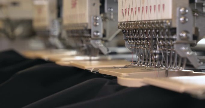 In slow motion video in a garment factory, a sewing machine embroiders various companies and engravings. Concept of: Automated work, Sewing machine, Engraving, Thread, Fabric, Needle.