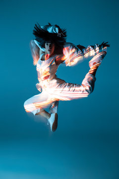 Pretty young woman in sportswear leaping up and looking at camera on blue background