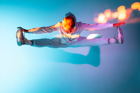 Unrecognizable man in sportswear spreading legs and jumping high in air near bright specks of light