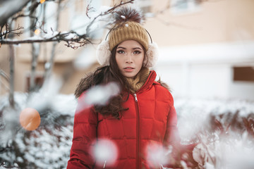 gorgeous filipino asian girl in her 30s standing out in the snow showing her beautiful eyes and long curly hair staring at the cam while wearing a beanie hat and earmuffs with a red jacket in Iceland  - obrazy, fototapety, plakaty