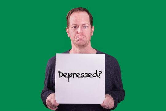 Red haired middle aged freckled adult male frowning holding sign with the word Depressed? captured on green screen background 