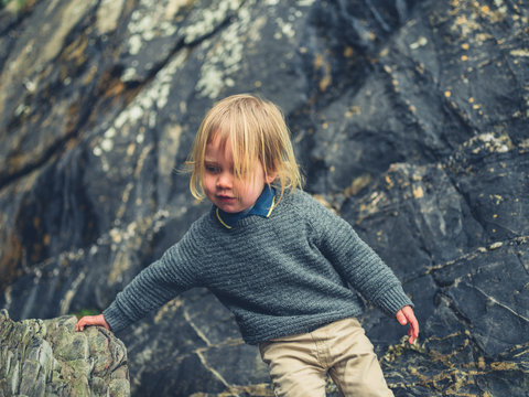 Little toddler climbing on rocks on the beach