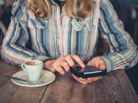 Young woman drinking coffee and using smartphone