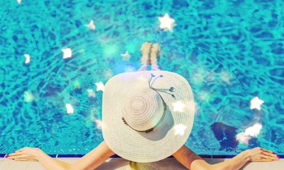 Beautiful woman in a hat sitting on the edge of the swimming pool