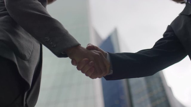 Two Asian business men's hands come together for a handshake in the city, in slow motion