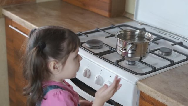 Life threatening. A little girl is touching a hot pot on the stove.