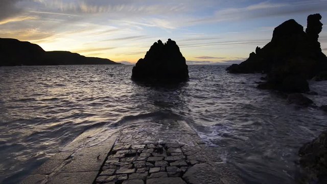 Dramatic sunset over sea stacks and an old stone jetty at Pettico Wick Bay at St Abbs in the Scottish Borders
