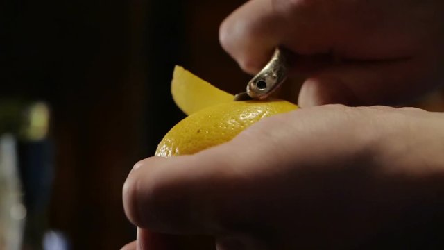The bartender cuts the zest from the lemon for a cocktail, close-up