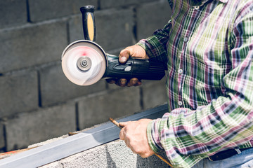 Close up on man using grinder to cut metal bar at the construction site