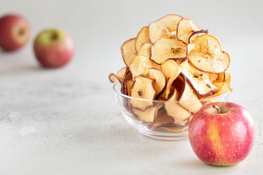 Hipped Dried apple chips in glass bowl with fresh apple in foreground on light background - Image