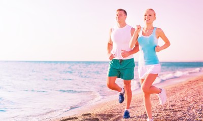 Couple running. Sport runners jogging on beach working out smiling happy. Fit male fitness model and attractive female jogger. Multiracial group, Asian woman and Caucasian man