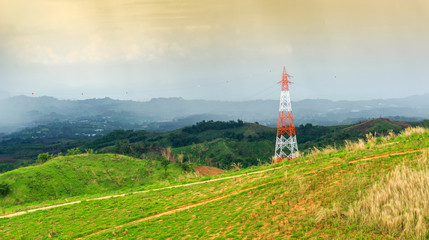 High voltage electric tower on green field with mountains in rural Produce electricity to supply electricity to industrial in city in the evening time.