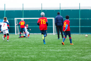 Boys kick soccer ball. Footballers run after the ball on green grass. Kids in white and red shirts dribbling, improve  skills. Training, football, hobby, active lifestyle