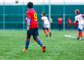 Boys kick soccer ball. Footballers run after the ball on green grass. Kids in white and red shirts dribbling, improve  skills. Training, football, hobby, active lifestyle