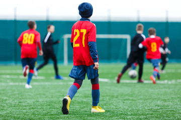 Obraz premium Boys kick soccer ball. Footballers run after the ball on green grass. Kids in white and red shirts dribbling, improve skills. Training, football, hobby, active lifestyle