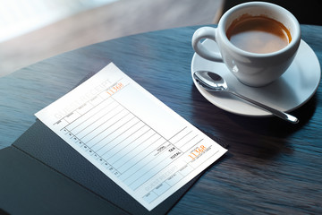 Close up of cheque and coffee cup on wooden table in modern cafe. 3d rendering.