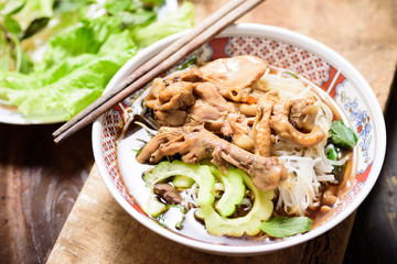 Rice noodles soup with stewed chicken wing and feet in a bowl with chopsticks