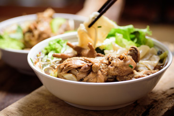 Hand holding chopsticks for eating rice noodles soup with stewed chicken wing and feet in a bowl