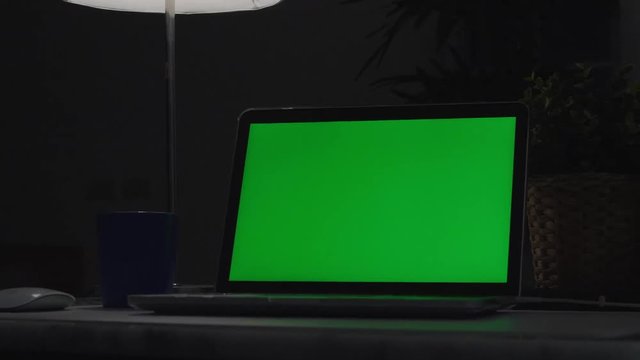 Laptop with green screen. Dark office. Dolly shoot. Perfect to put your own image or video.Green screen of technology being used. Chroma Key laptop