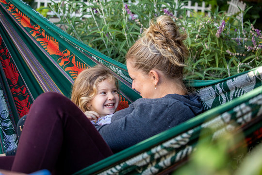 A mother and daughter relaxing while swinging in a hammock together. 