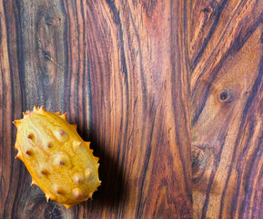 An exotic kiwano fruit on the bottom left of a wooden backdrop