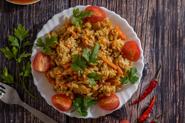 Pilaf and cherry tomatoes in plate on wooden background. Central Asian cuisine. Horizontal orientation. Hot peppers