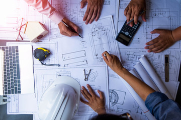 engineers pointing to building on blueprint and using laptop to drawing design building Project in office, construction concept. Engineer concept