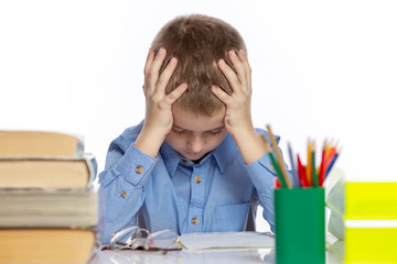 Cute sad schoolboy sitting at the table with books and notebooks. Tired of doing homework. Isolated on a white background. Close-up.